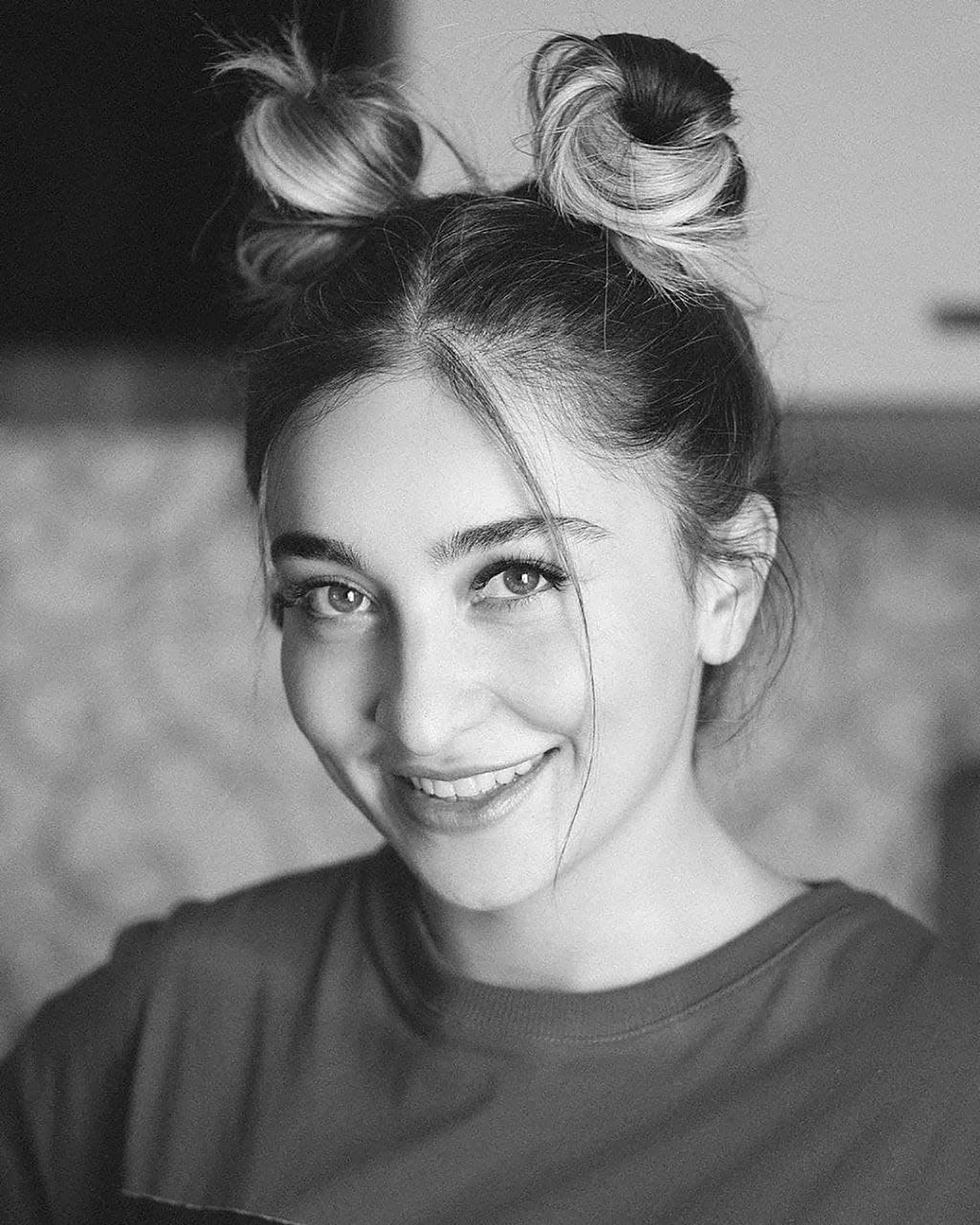 Monochrome portrait of a smiling woman with hair buns, exuding happiness.